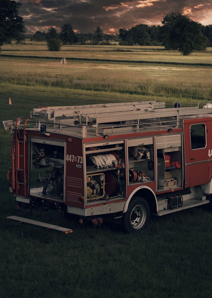 Home A fire truck stands ready against a dramatic sunset in a rural field, symbolizing safety.