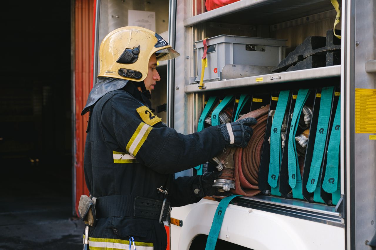Home A firefighter in full gear organizes hoses in a fire truck, demonstrating safety and preparedness.
